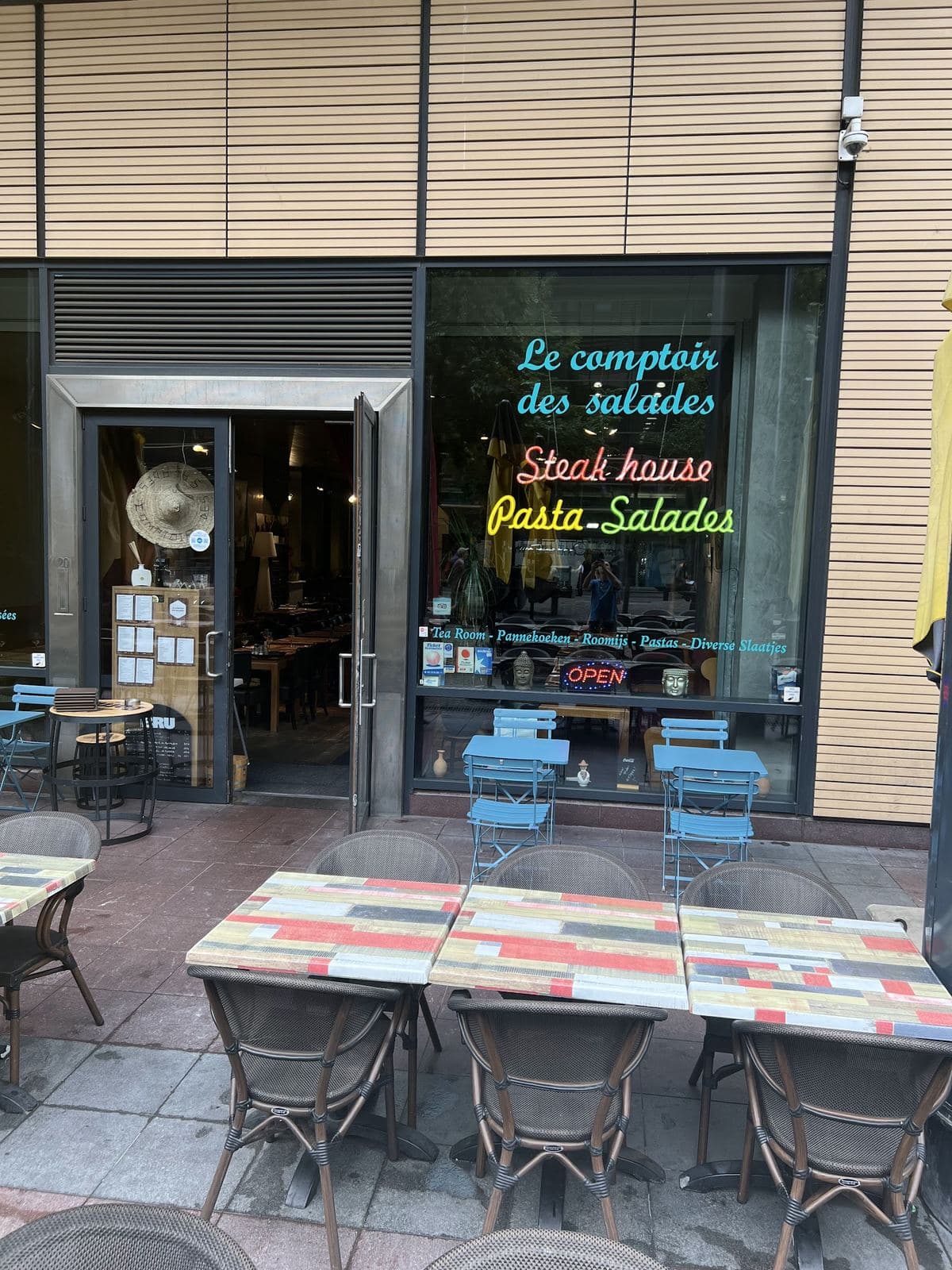 De gevel aan het Victor Hortaplein: de neonletters „Le comptoir des salades”, „Steak house” en „Pasta - Salades” in de etalage, met het terras en de kleurige tafels ervoor