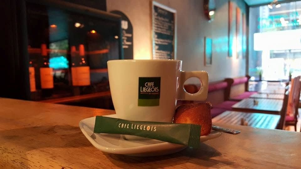 Een kop koffie op de houten toog; erachter de zaal, met tafels en rode banken langs de muur