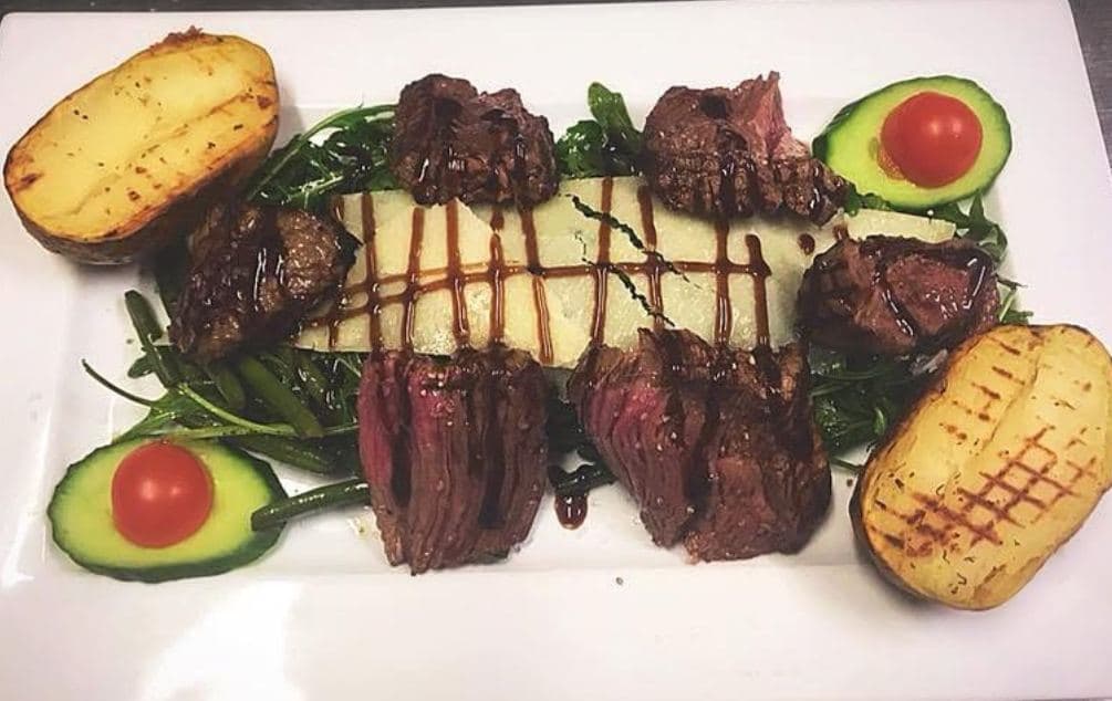 Medaillons gegrild rundvlees op een rij op rucola, tussen twee halve avocado's en twee gegrilde aardappelen