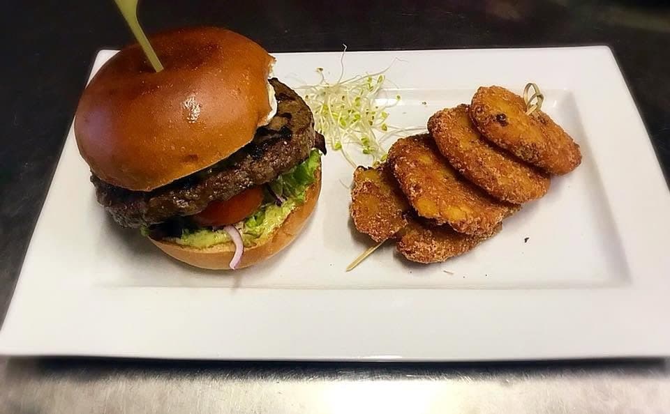 Un burger au pain brioché servi avec des croquettes, sur une assiette rectangulaire
