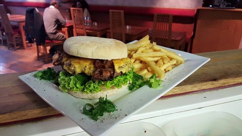 Un bacon cheeseburger et ses frites posés sur le comptoir en bois, la salle derrière