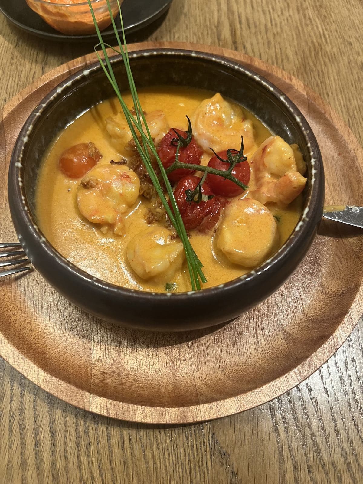 Sint-Jakobsvruchten en scampi's in een oranje saus, met geroosterde kerstomaten, in een zwart pannetje