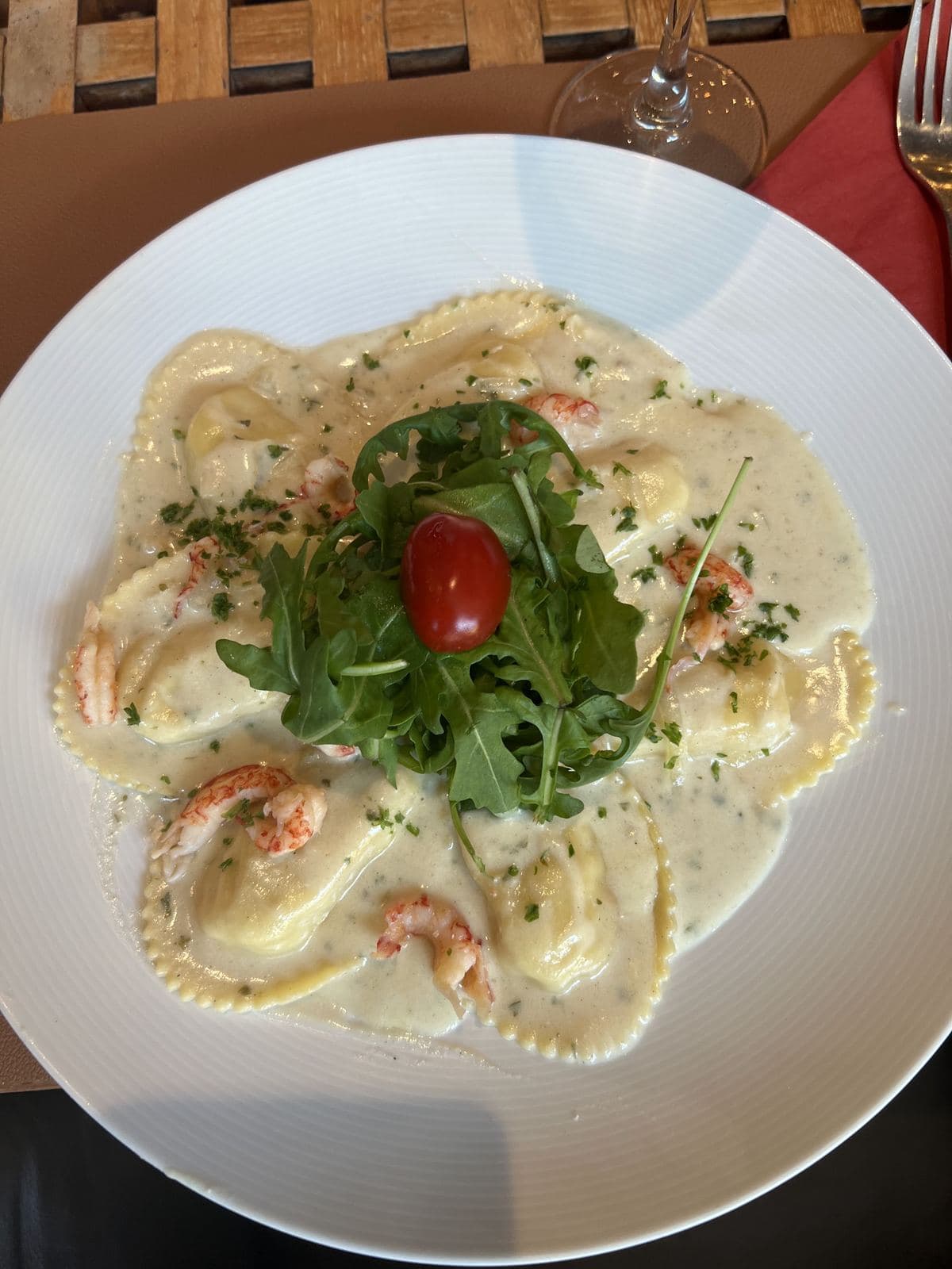 Ravioli in een romige saus met garnalen, onder een toefje rucola en een kerstomaat