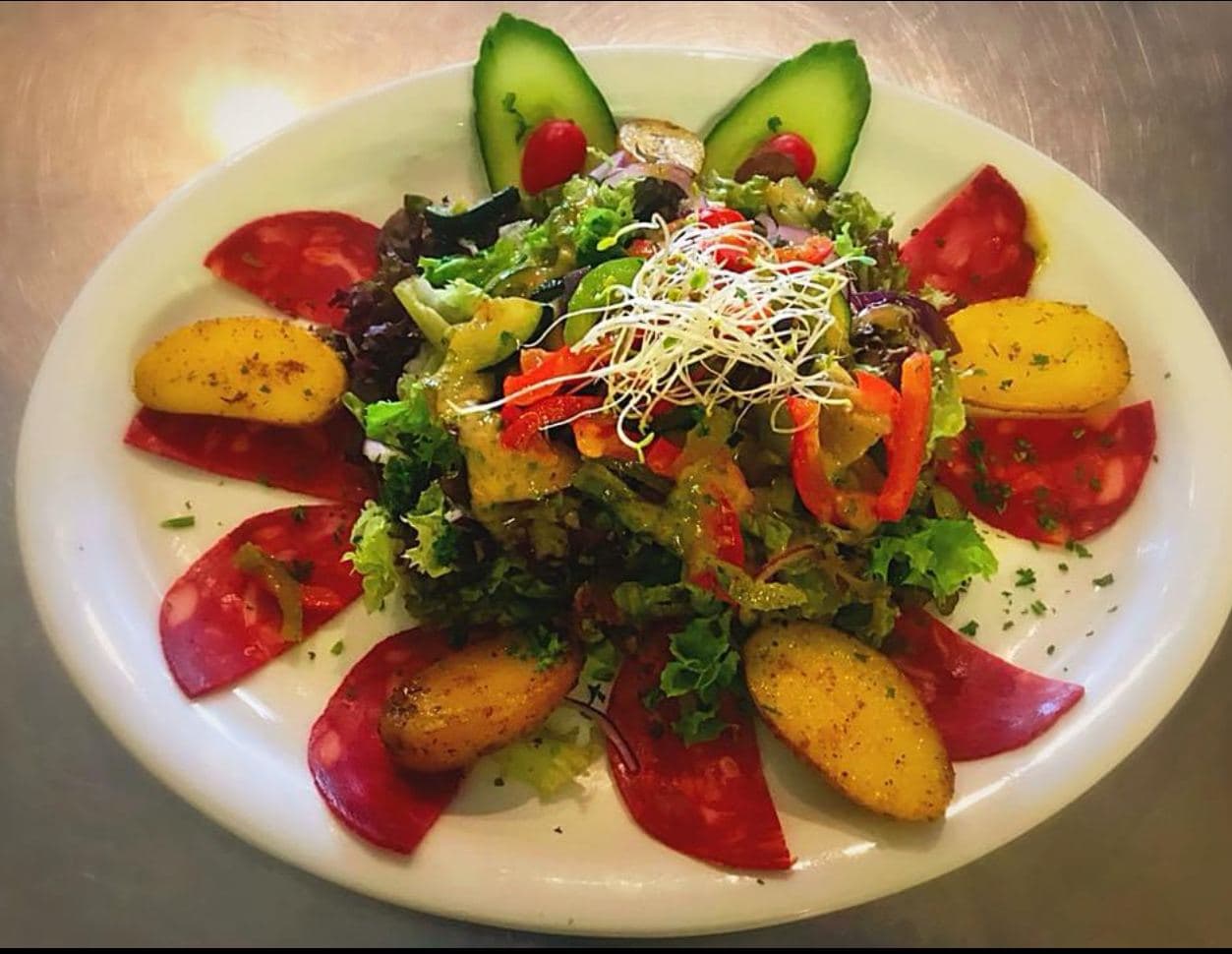 Une salade garnie de fines tranches de charcuterie, de pommes de terre rôties, de lamelles de poivron et de concombre