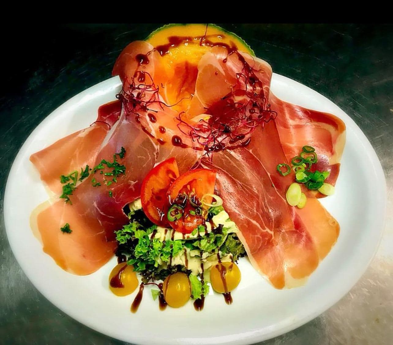 Rauwe ham en meloen in een waaier boven een groene salade en kerstomaten