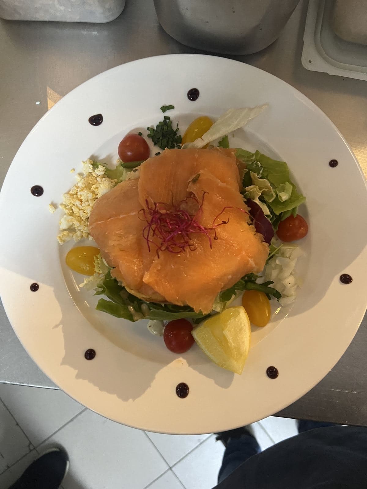 Du saumon fumé posé sur une salade, avec des quartiers d'agrumes et des tomates cerise, sur une assiette blanche