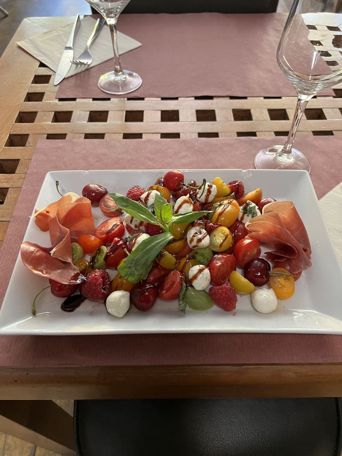 Kerstomaten in alle kleuren, mozzarellabolletjes en rauwe ham op een witte schaal, op het terras