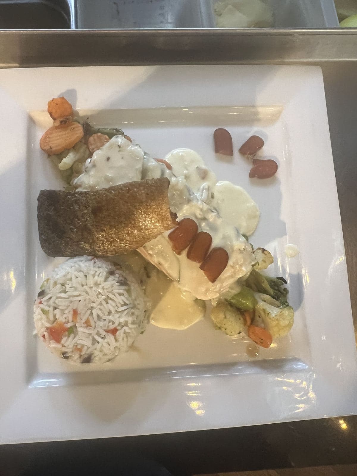 Un filet de poisson grillé, du riz aux petits légumes et des légumes en sauce, sur une assiette carrée