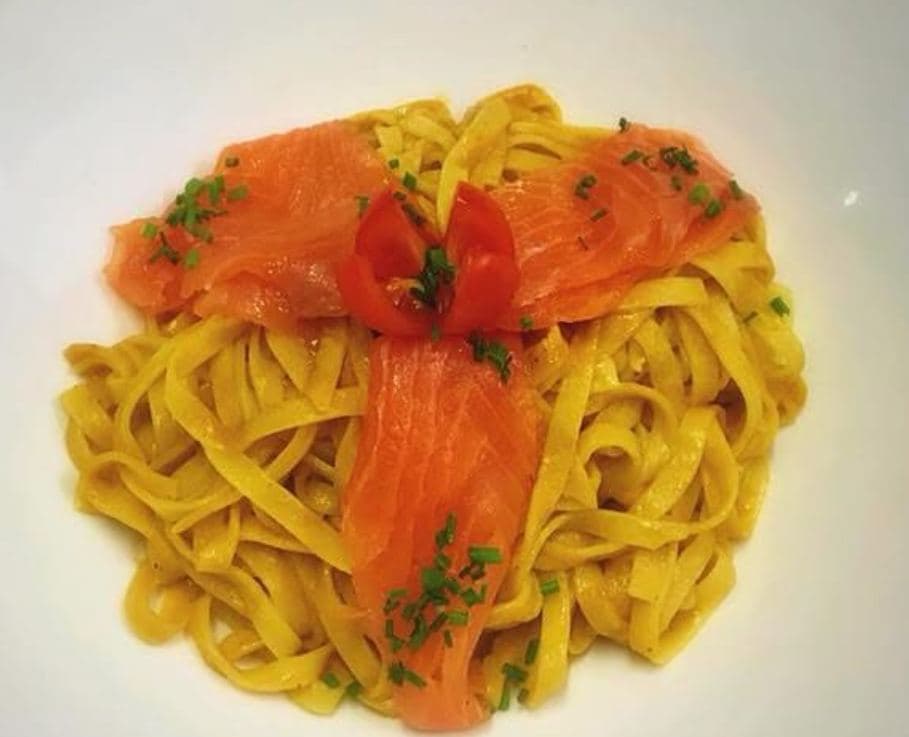 Een nestje tagliatelle bedekt met reepjes gerookte zalm en een tomatenroosje